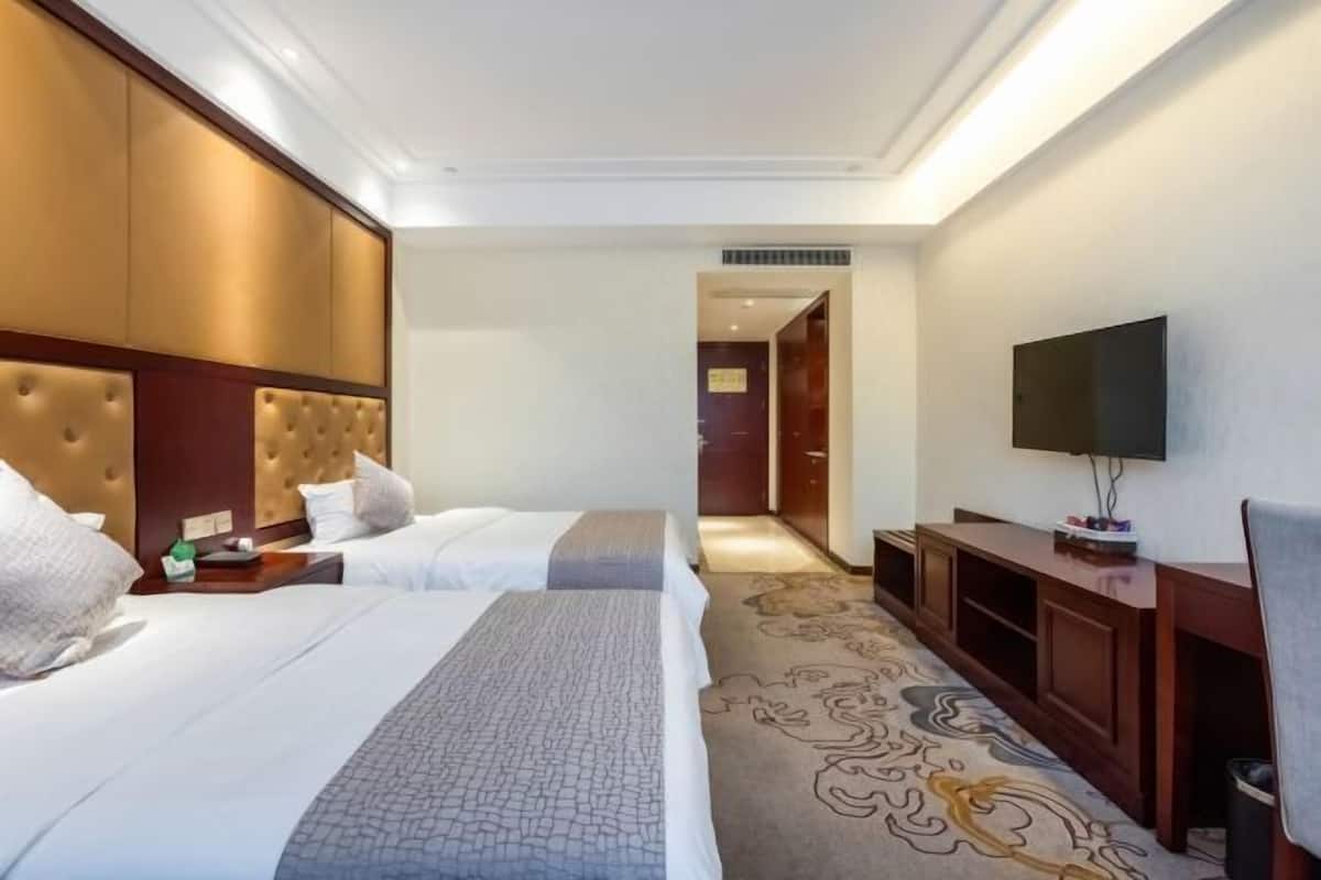 Habitación de hotel con dos camas, televisión, escritorio y piso alfombrado.