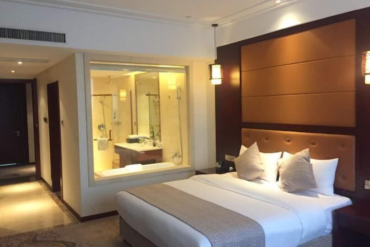 Habitación de hotel con una cama grande, una mesita de noche, un espejo y vista al baño.