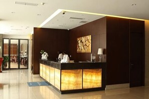 A reception desk with a modern design, a large abstract painting, and a door to the right. - Regan International Hotel (Wuxi)