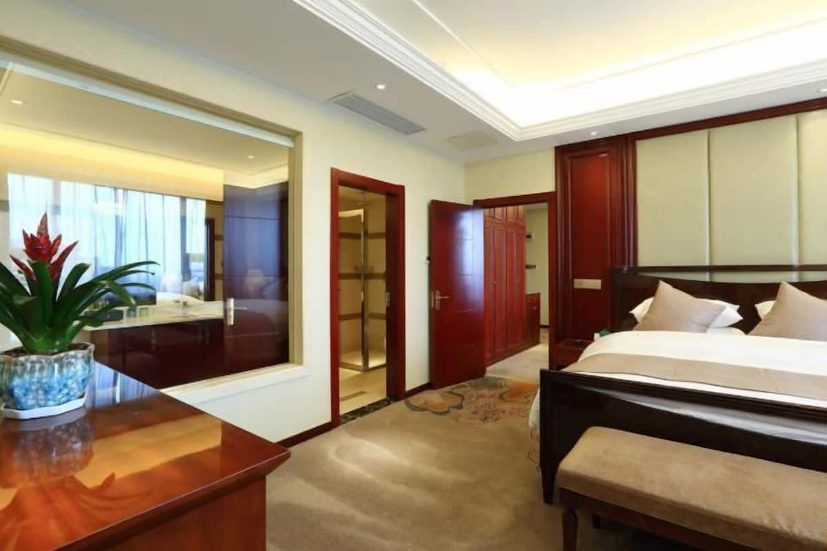 Habitación de hotel con cama, mesita de noche, espejo y planta en maceta.