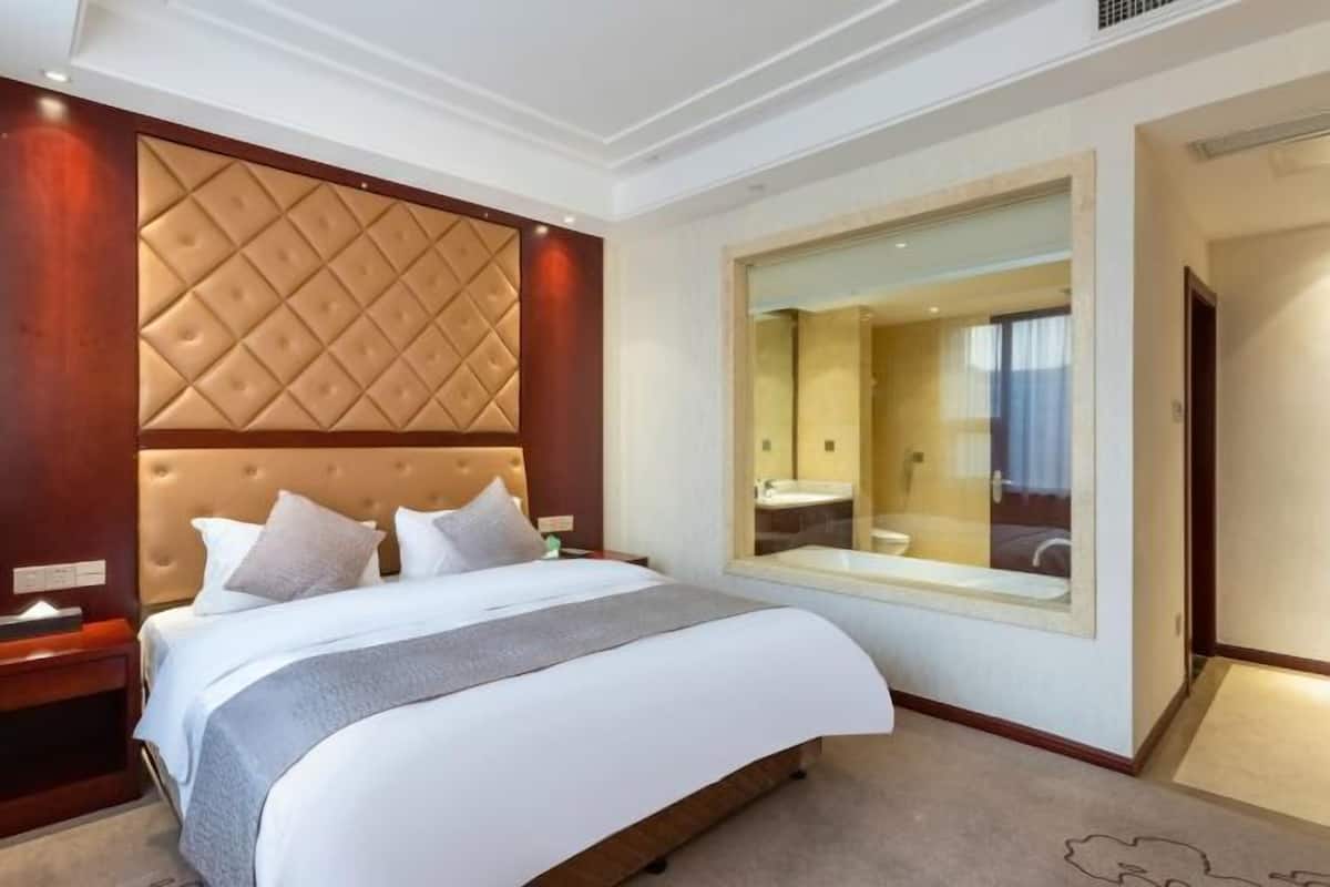 Habitación de hotel con una cama grande, un cabecero de madera, un espejo amplio y vistas al baño.
