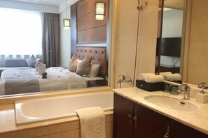 A hotel room with a large bed, a sitting area with a sofa, a bathroom with a bathtub, a sink, and a mirror. - Regan International Hotel (Wuxi)