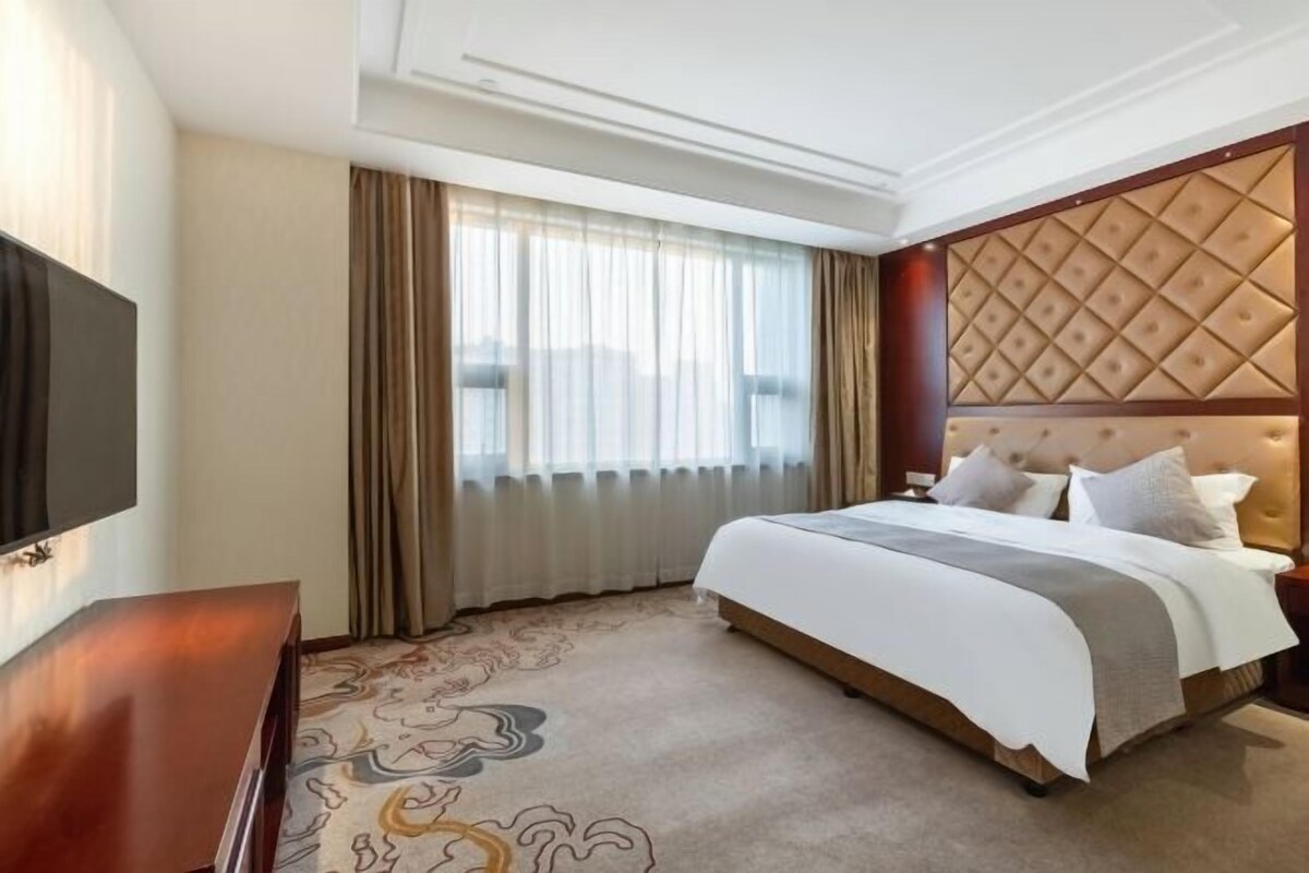 A hotel room with a large bed, a flat-screen TV, a wooden dresser, and a decorative carpet.