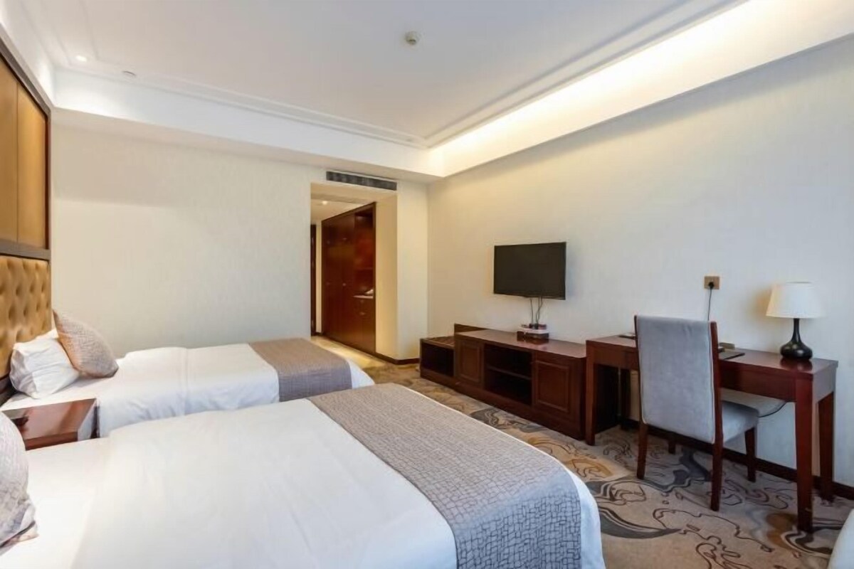 A hotel room with two beds, a TV, a desk, and a chair.