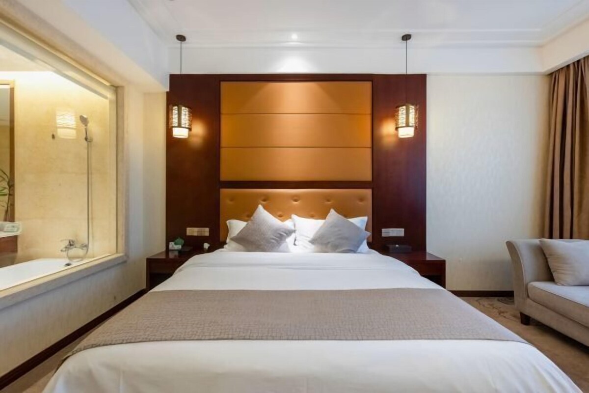 A hotel room with a large bed, bedside lamps, a nightstand, a sofa, and a bathroom with a shower.