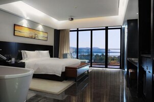 Una habitación de hotel moderna con una cama grande, una televisión de pantalla plana, un baño con bañera y un balcón con vistas a las montañas.