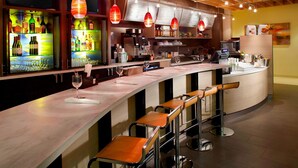 Zona de bar con una barra alargada, varios taburetes y lámparas colgantes rojas.