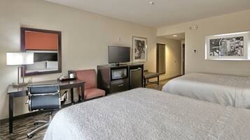 A hotel room with two beds, a desk with a chair, a television, and artwork on the walls.