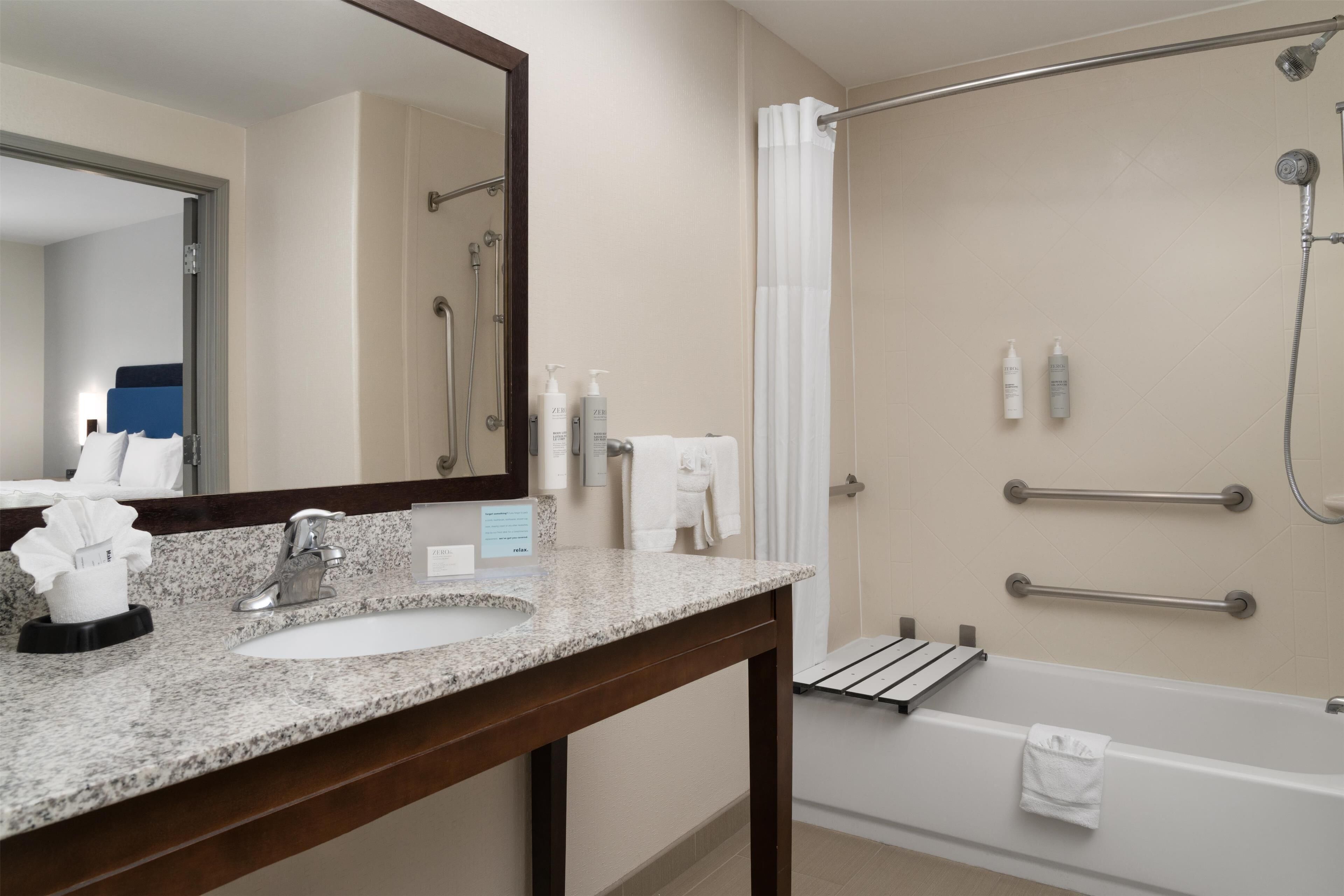 Un baño con lavabo, espejo, ducha y dos botellas de champú.