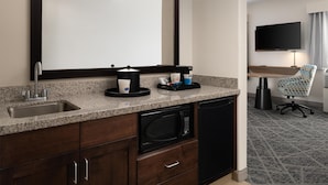 A hotel kitchenette with a microwave, sink, and cabinets. There is a chair and a TV in the background. - Hampton Inn & Suites Albuquerque North/I-25 (Albuquerque)
