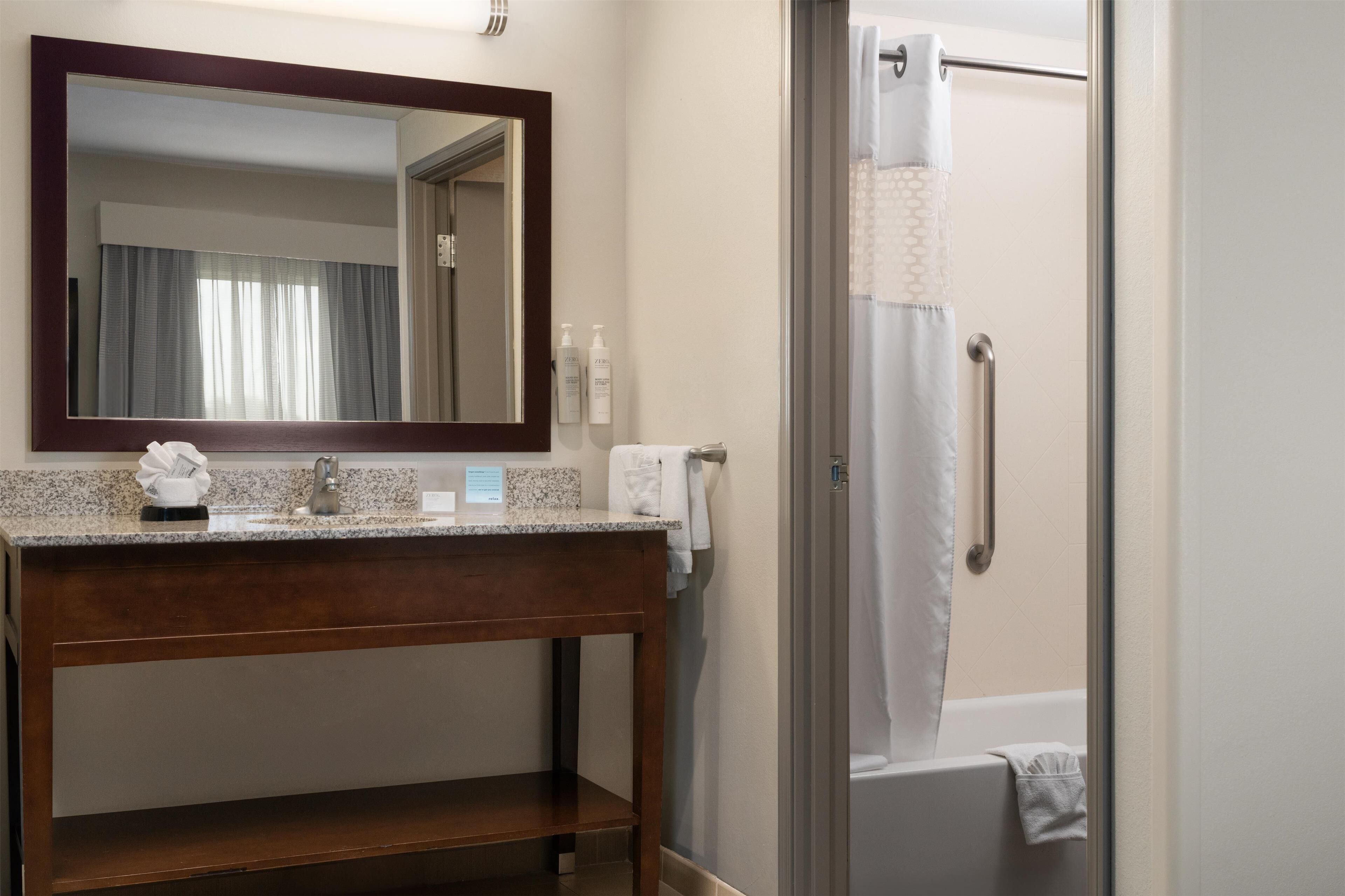 Une salle de bain dotée d’un comptoir en granit, d’un meuble-lavabo en bois, d’un miroir, d’une douche avec une porte en verre et d’un porte-serviettes.