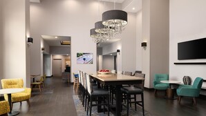 A modern hotel lobby with a central dining area, a reception desk, and a large TV screen. - Hampton Inn & Suites Albuquerque North/I-25 (Albuquerque)