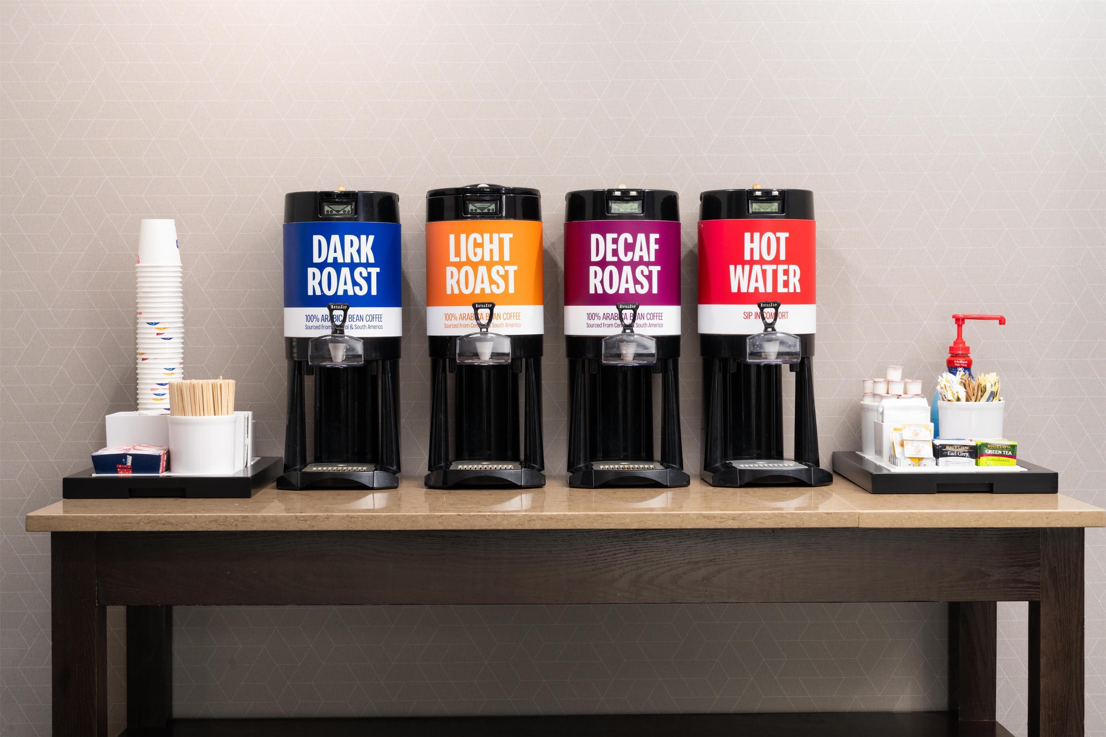 Eine Kaffeestation mit vier Spendern, beschriftet mit 'DARK ROAST', 'LIGHT ROAST', 'DECAF ROAST' und 'HOT WATER'.