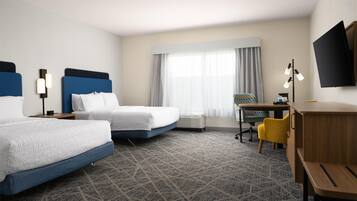 A hotel room with two beds, a desk, a chair, a TV, and a large window with curtains.