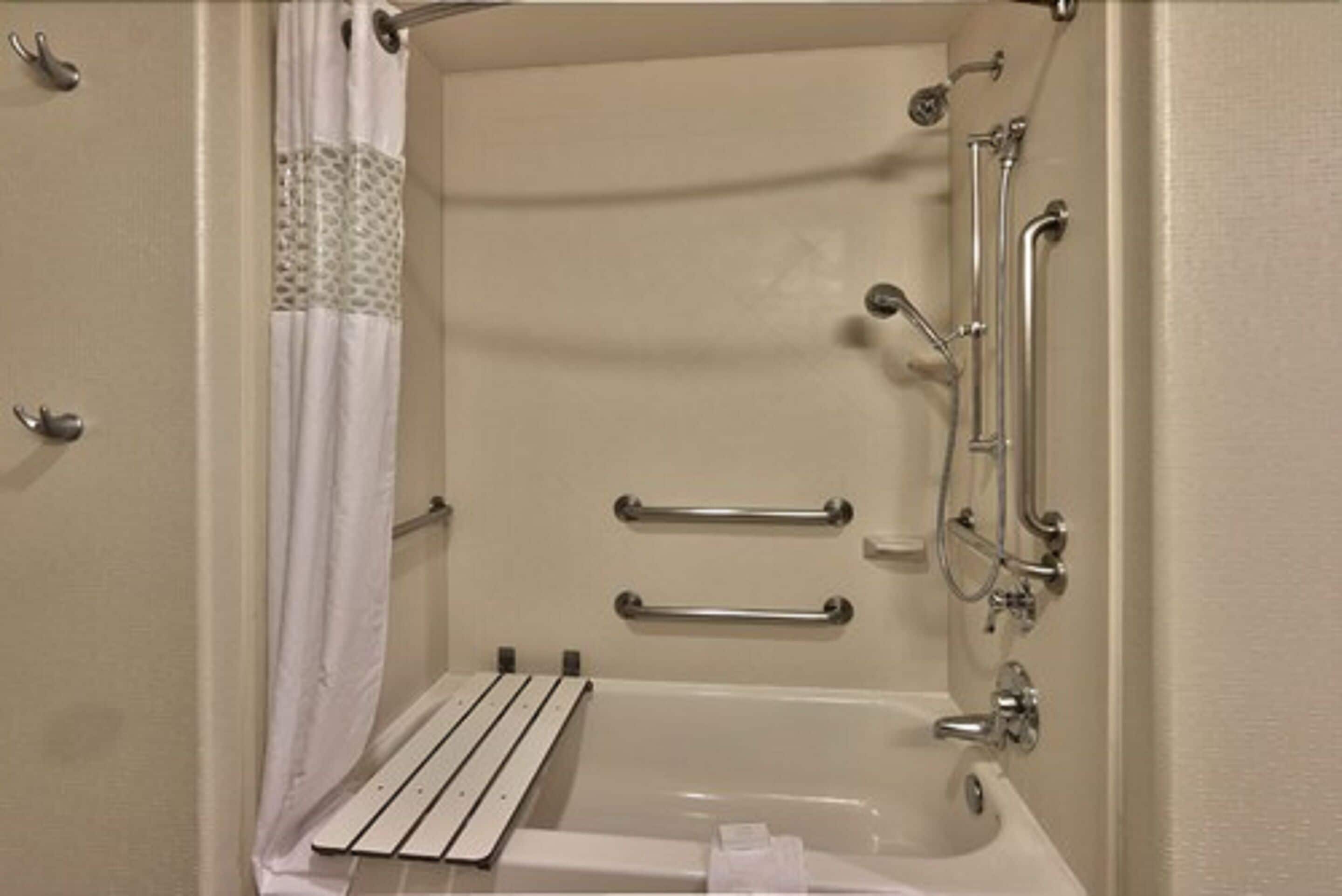 A bathroom with a bathtub, grab bars, a showerhead, and a towel rack.