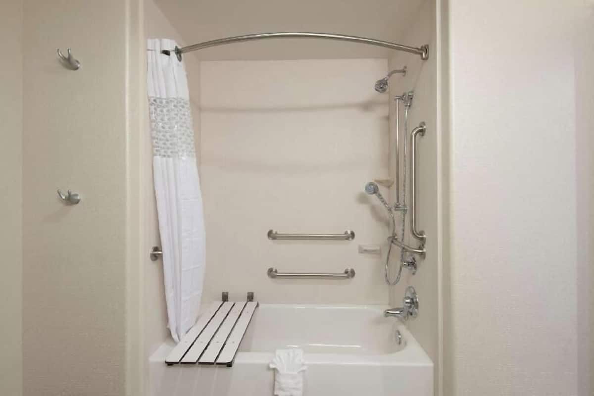 Un baño con bañera, ducha y barras de apoyo.