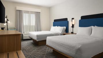 A hotel room with two beds, a desk, a lamp, and a window with curtains.