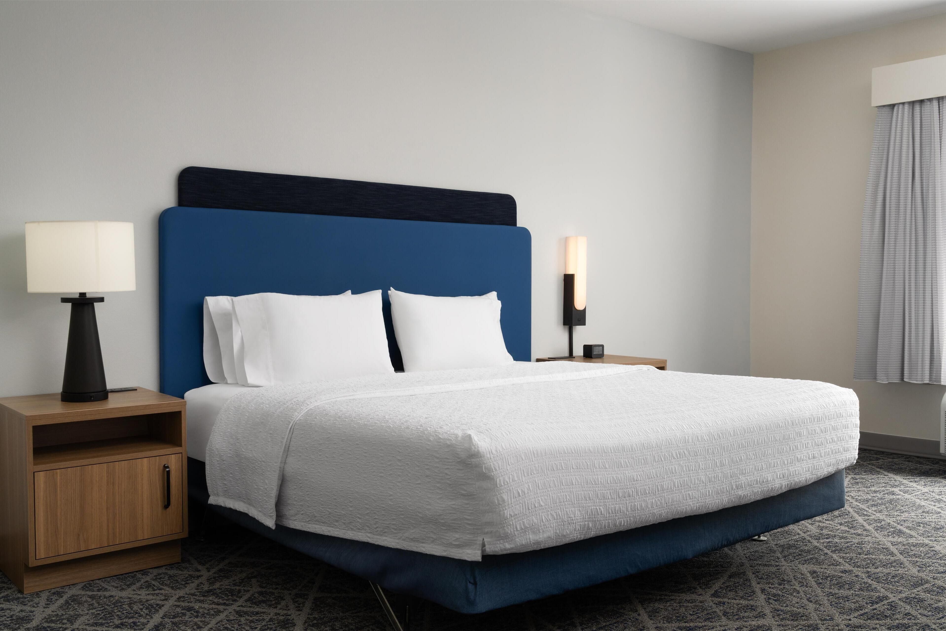 A neatly made bed with a blue headboard, a bedside table with a lamp, and a nightstand with a candle.