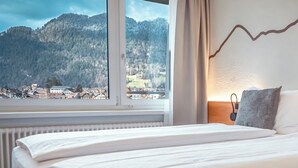 Una habitación de hotel con una cama grande, vista a un paisaje montañoso y una lámpara fijada a la pared.