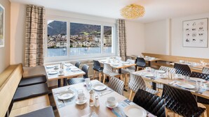 Comedor con mesas dispuestas para comidas, sillas y vista a un lago y edificios.