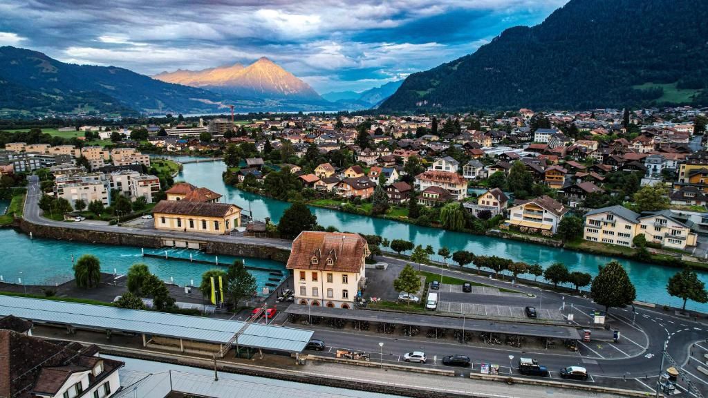 Una cittadina con un fiume, un edificio importante dal tetto rosso e montagne sullo sfondo.