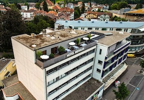 A multi-story hotel with a rooftop terrace and a sign reading 'HOTEL MERKUR.'