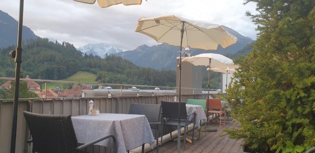 An outdoor terrace with tables and chairs, a view of mountains, and a tree.