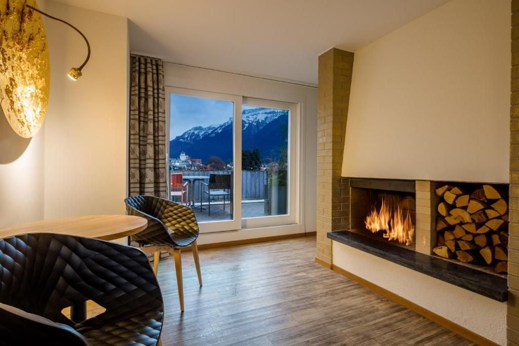 Una sala de estar moderna con chimenea, un comedor con mesa y sillas, y un ventanal con vistas a la montaña.