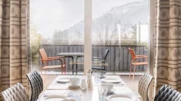 A dining area with a table set for four, chairs, and a view of a mountain through large windows.