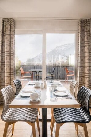 Un comedor con una mesa dispuesta para cuatro personas, sillas y vistas a la montaña a través de amplios ventanales.