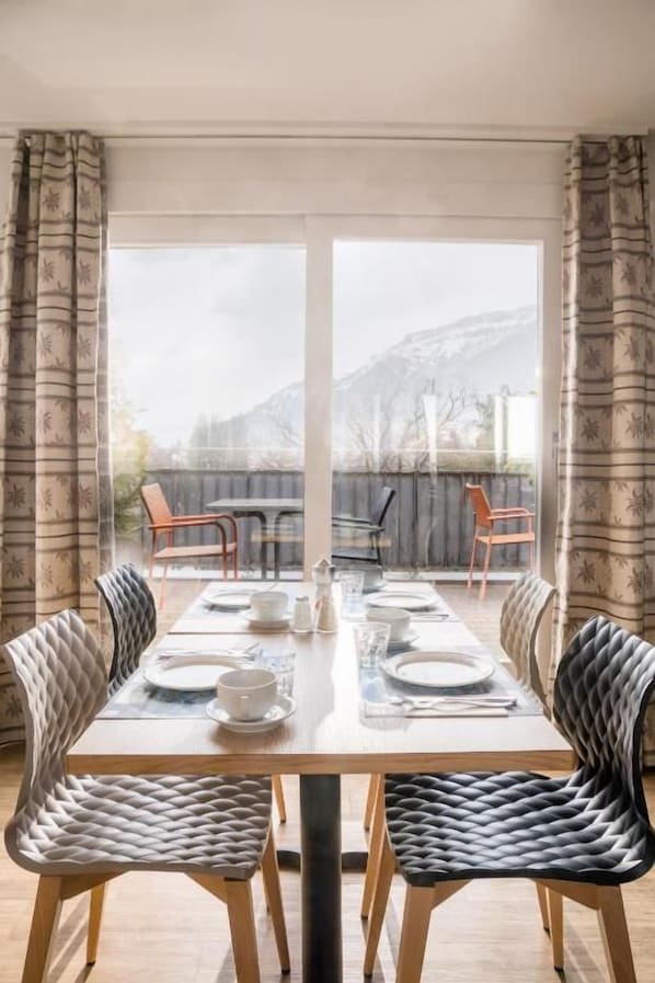 Un comedor con una mesa dispuesta para cuatro personas, sillas y vistas a la montaña a través de amplios ventanales.