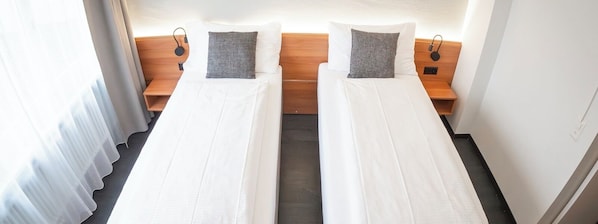 Habitación de hotel con dos camas individuales, cabeceros de madera y mesitas de noche con lámparas.