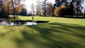 Campo de golf con un estanque, árboles y una bandera que marca el hoyo número 5.