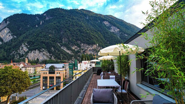 Una terraza exterior con mesas y sillas, con vistas a un paisaje montañoso.