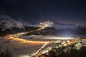 A snow-covered mountain landscape at night with a town and a lake in the foreground.