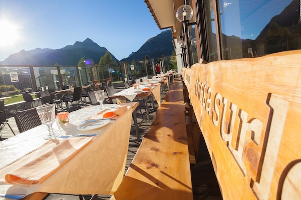 An outdoor dining area with tables set for two, overlooking a mountainous landscape.