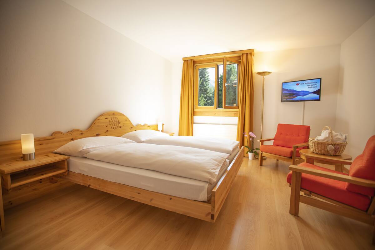 A room with a wooden bed, a TV on the wall, and a window with curtains.