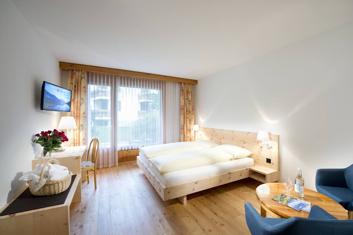 A hotel room with a bed, a desk with a lamp, a chair, a TV, and a window with curtains.