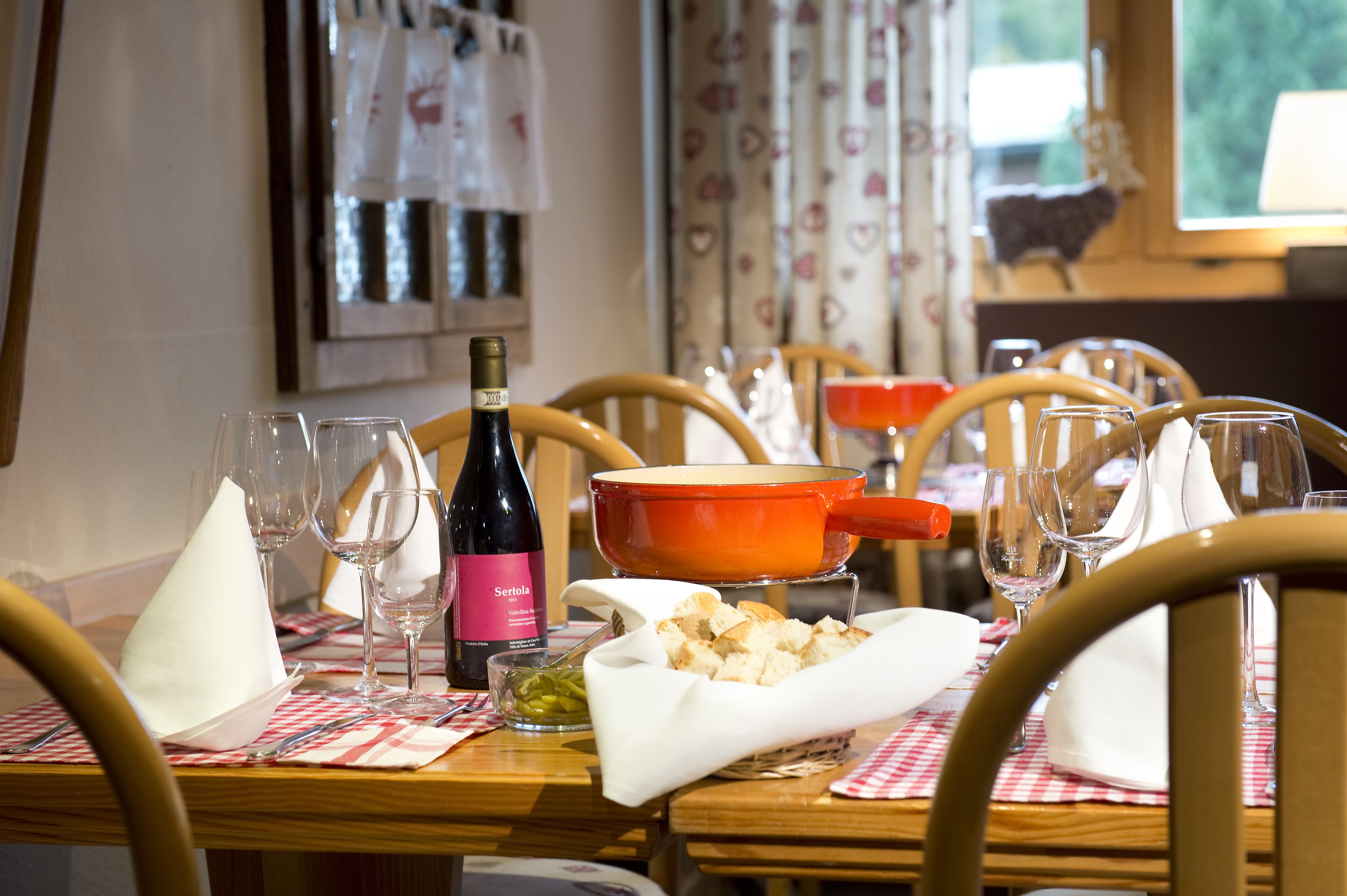 A dining table set with wine glasses, a bottle of wine, a bowl of bread, and a small dish of olives.