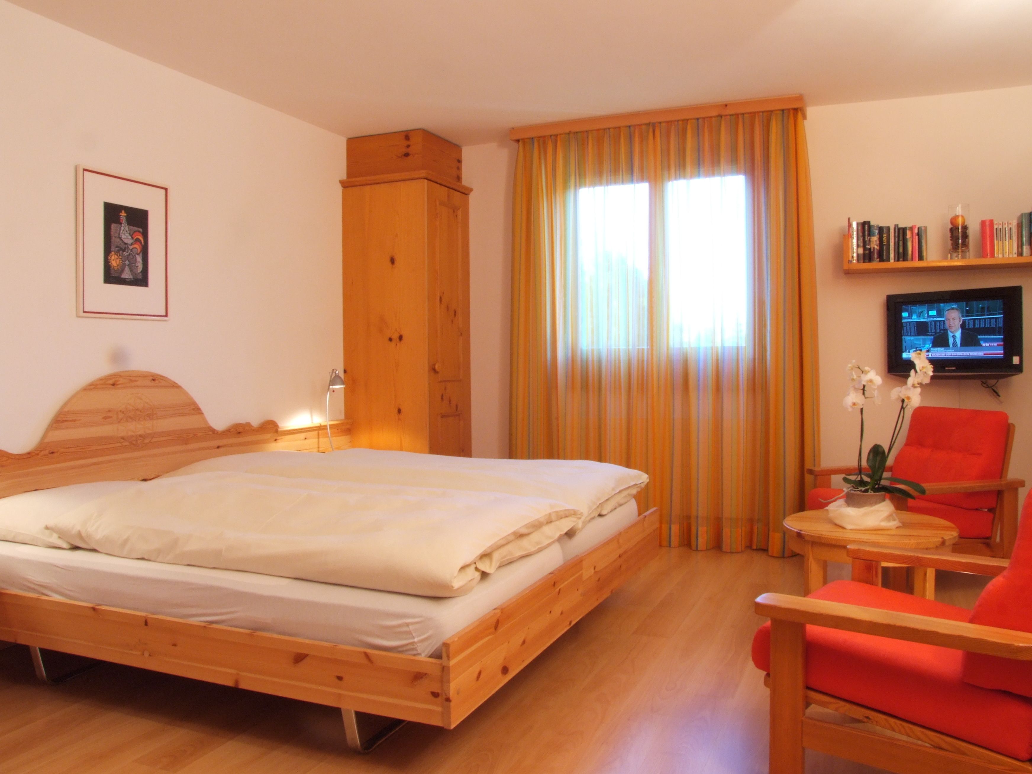 Un dormitorio con una cama de madera, una silla, un televisor y una estantería.