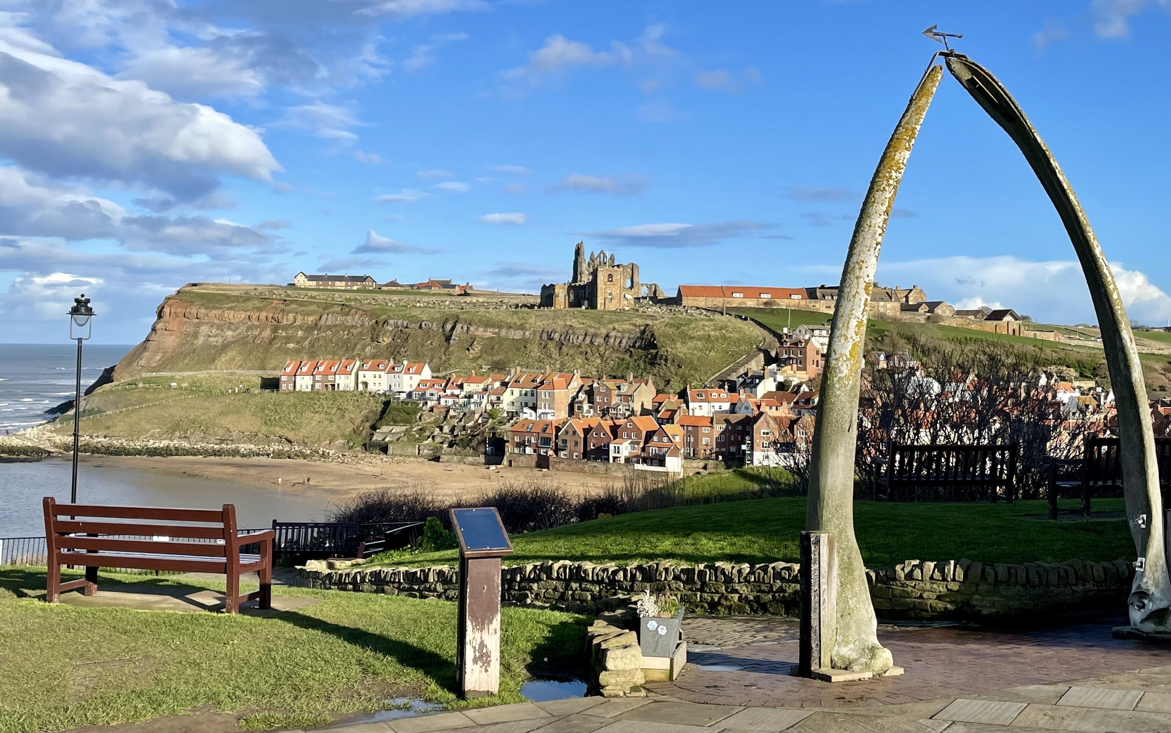 Une ville côtière dotée de bâtiments historiques, d’une imposante structure en forme d’arc et offrant une vue sur la mer.