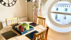 A dining area with a round table, chairs, a clock, a window with a view, and a ceiling light. - Fayvan Apartments (Whitby)