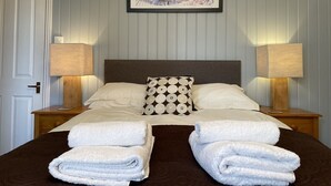 A neatly made bed with two pillows, two bedside lamps, and two folded towels. - Fayvan Apartments (Whitby)