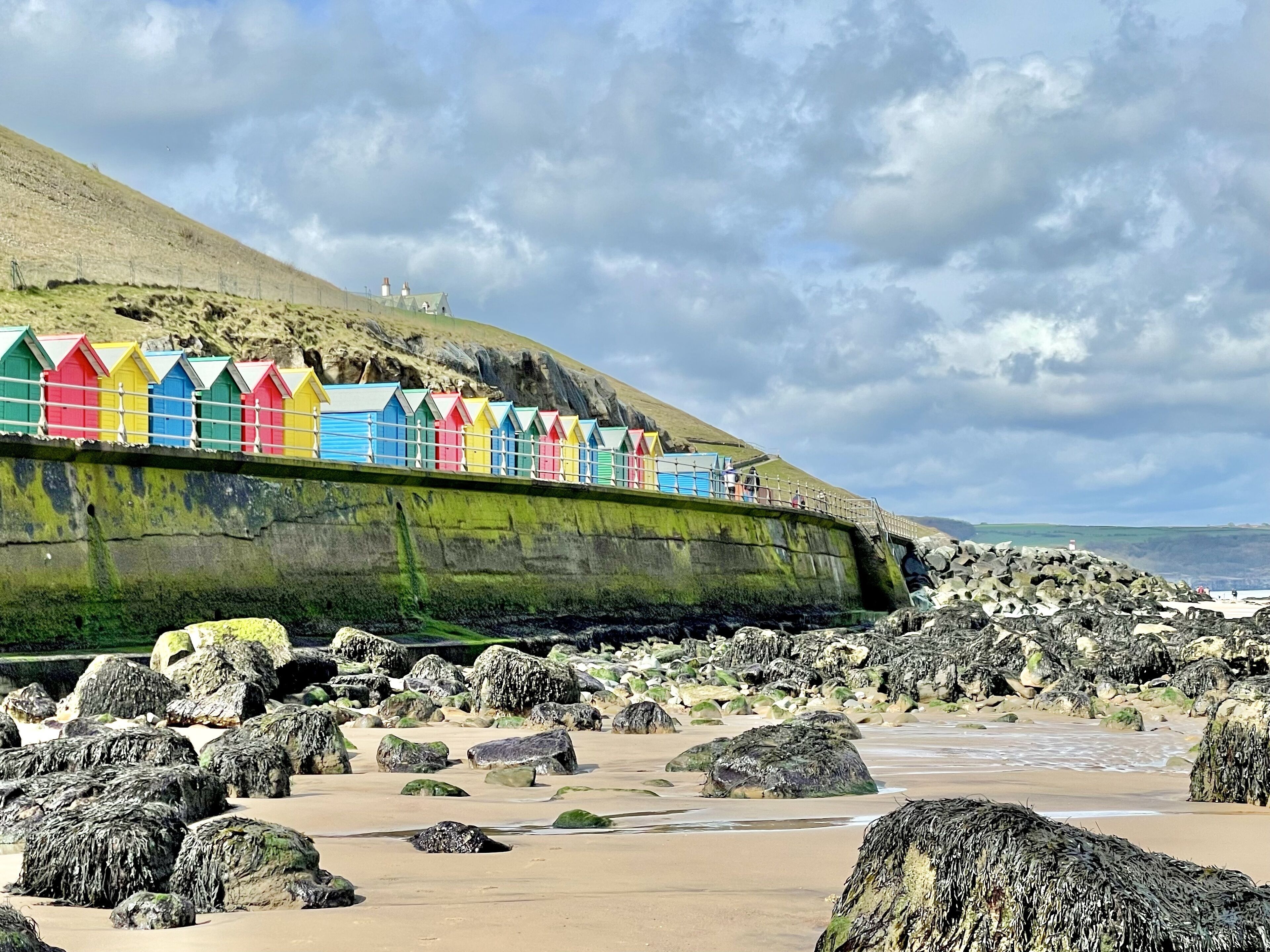 A beach with colorful beach huts and a large green shipwreck.