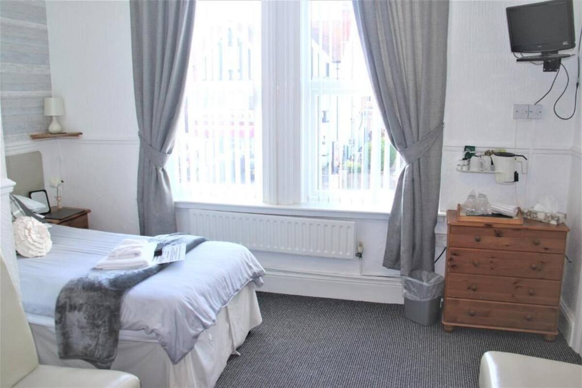 A hotel room with a bed, a dresser, a TV, and a window with curtains.