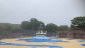 A water park with a central fountain, surrounded by blue and yellow pools, and a metal fence in the foreground. - Serena Court Hotel (Skegness)