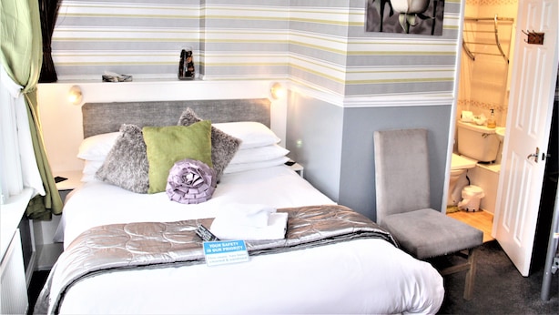 A hotel room with a striped wall, a bed with pillows, a chair, and a bathroom visible through an open door. - Serena Court Hotel (Skegness)