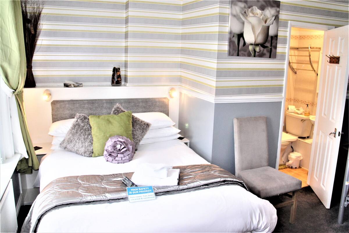 A hotel room with a striped wall, a bed with pillows, a chair, and a bathroom visible through an open door.