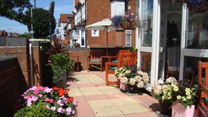A patio area with a tiled floor, wooden chairs, and potted plants. - Serena Court Hotel (Skegness)