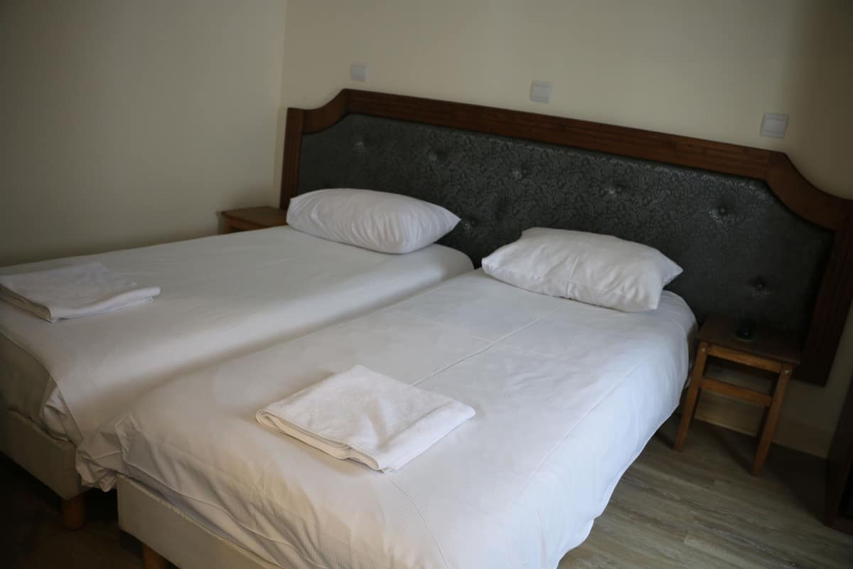 Cama doble con ropa de cama blanca y cabecera de madera. Hay dos mesitas de noche, una a cada lado de la cama.